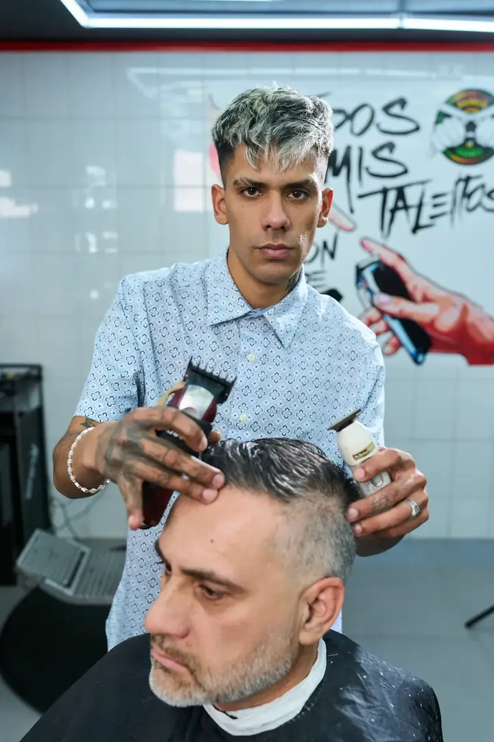 Barbero de El Ñaño con máquina de corte frente al mural del local